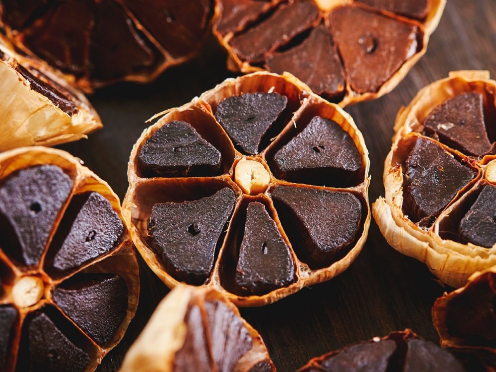 Halbierte Knoblauchknollen. Der Inhalt der einzelnen Kammern ist durch Fermentation rötlich-schwarz, glänzend und geleeartig.