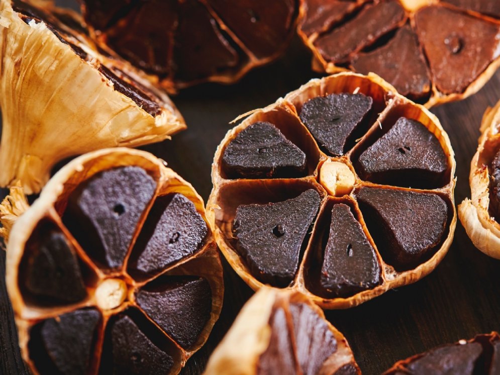 Halbierte Knoblauchknollen. Der Inhalt der einzelnen Kammern ist durch Fermentation rötlich-schwarz, glänzend und geleeartig.