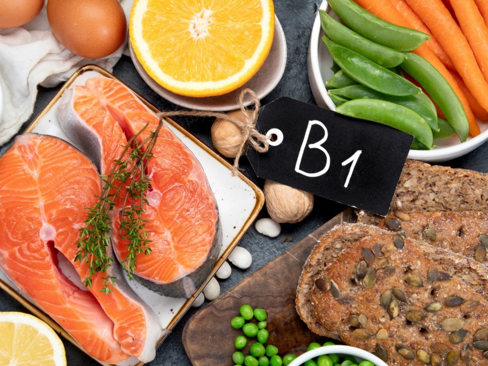 Verschiedene Teller und Schüsseln mit Lebensmitteln, wie Lachs, Erbsen, Walnüssen und Vollkornbrot, die reich an Vitamin B1 sind.